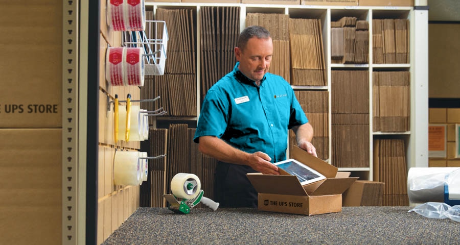 Male The UPS Store associate packing a tablet into a The UPS Store box